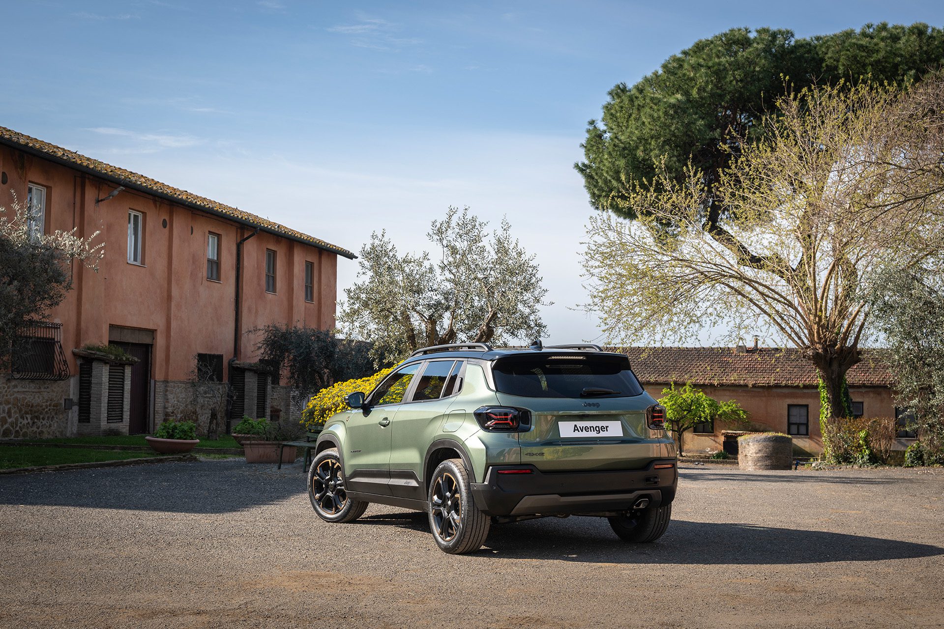 Groene Jeep Avenger 4xe schuin van achteren bij een landelijk gebouw