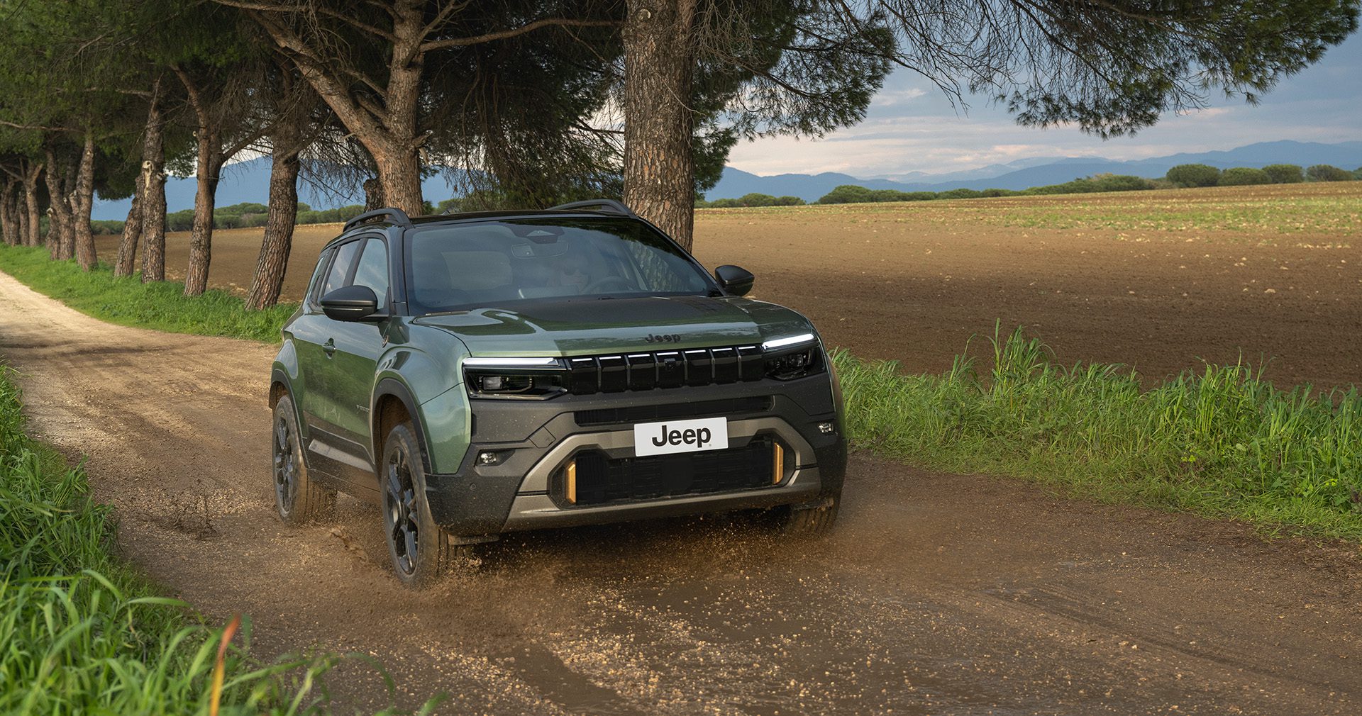 Groene Jeep Avenger 4xe rijdt over een onverharde weg tussen bomen