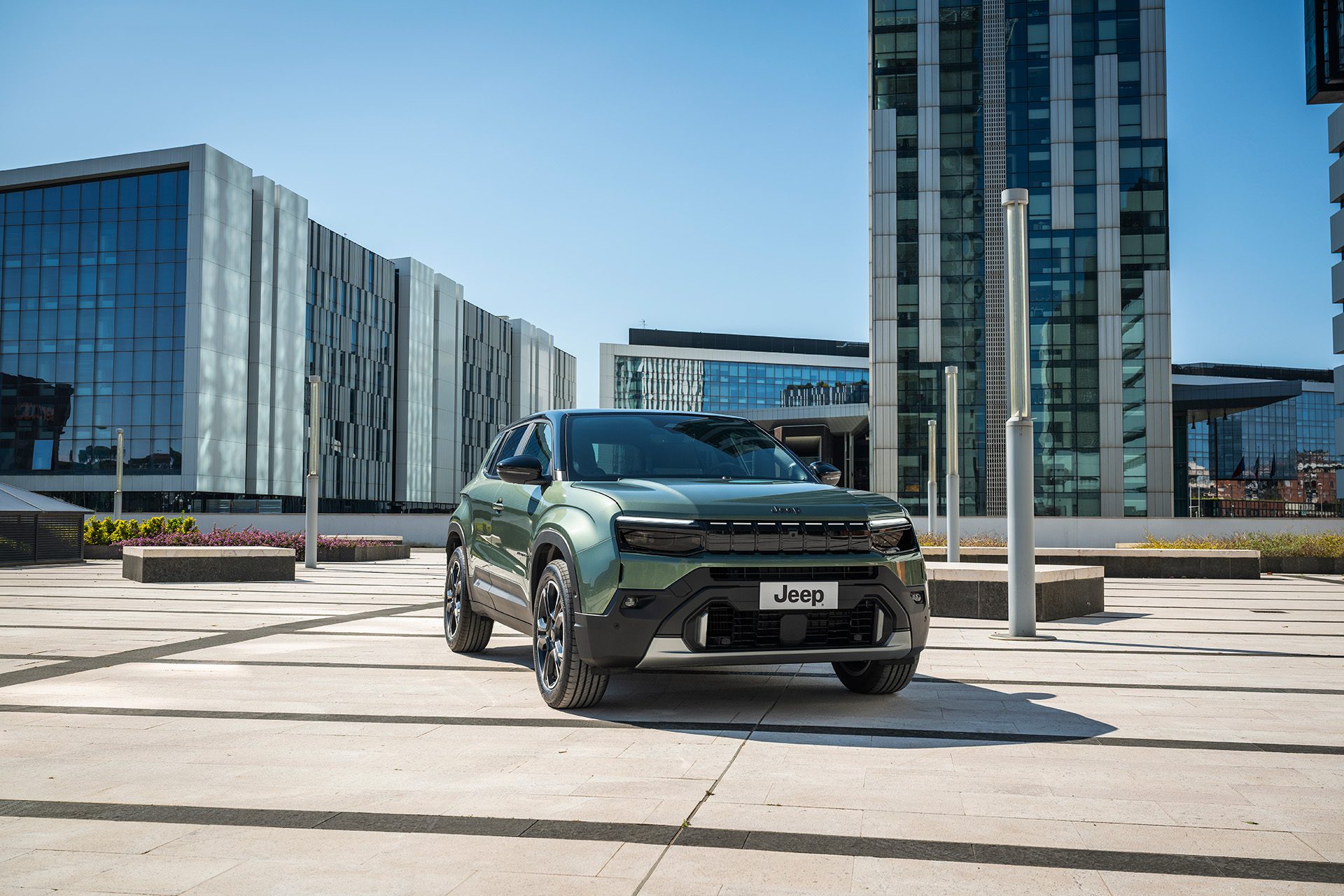 Groene Jeep Avenger Full Electric schuin van voren op een modern stadsplein