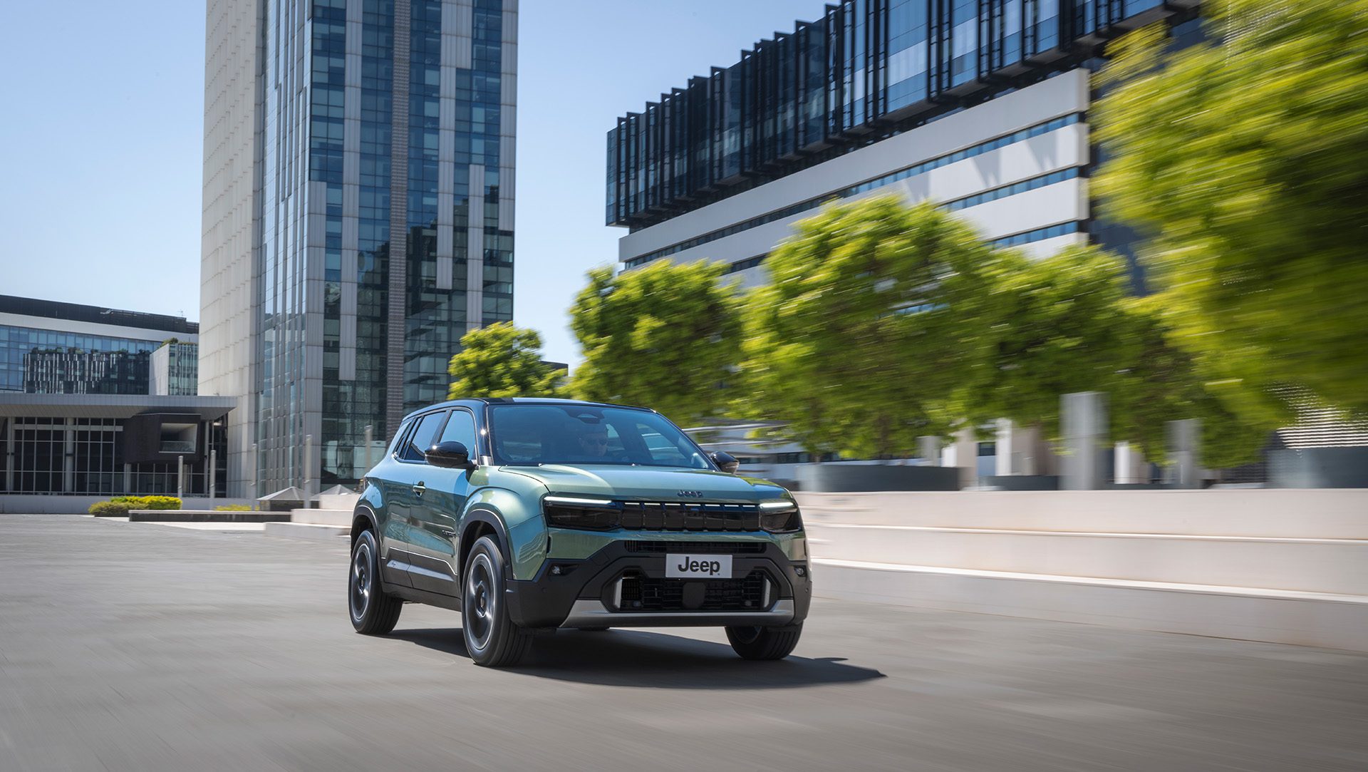 Groene Jeep Avenger Full Electric rijdt door een moderne stadsomgeving